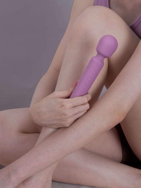 Elegancki masażer SVAKOM Mini Emma Neo w kobiecej dłoni na tle satynowej pościeli.